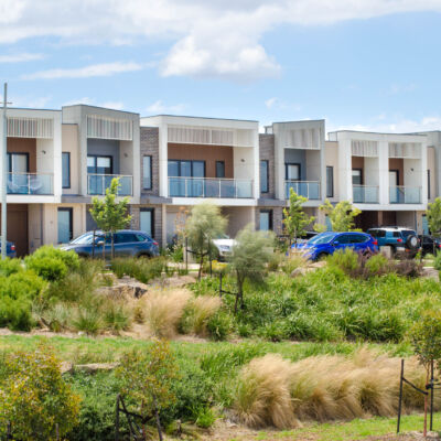 A row of residential townhouses with family cars parked at the front. Modern Australian homes in a new suburb. Concept of residence, real estate development, housing, population, and home ownership.