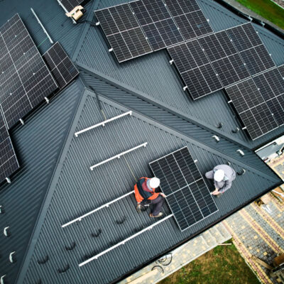 Men workers installing solar panels on roof of house.